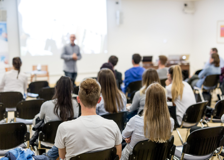 student seated in a lecture listening to person at front of room